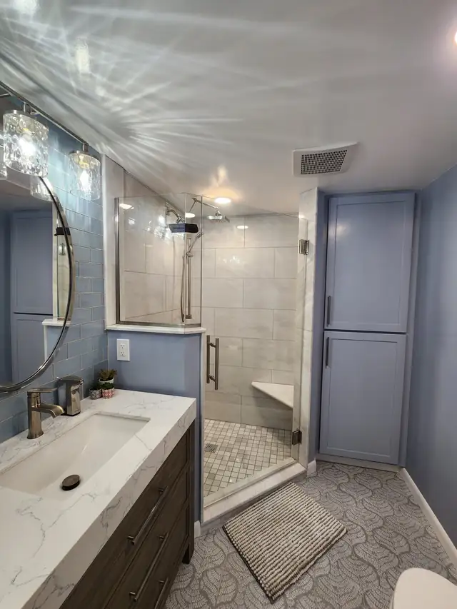 Bathroom remodel with blue-gray walls, a tiled walk-in shower, painted linen cabinet and round mirror