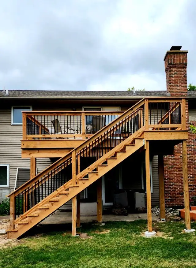 Two-story wood deck by JBJ with black metal railings and stairs on a brick home