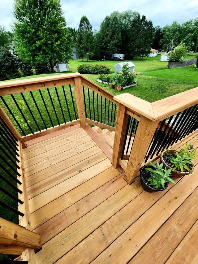 Wood deck with black metal balusters overlooking a green lawn and garden beds