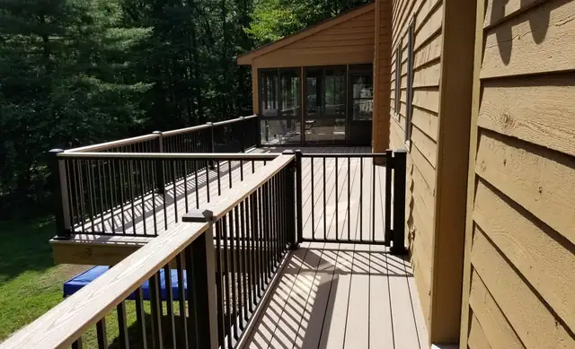 Elevated deck by JBJ with black metal railings and wood siding, looking out over a wooded yard