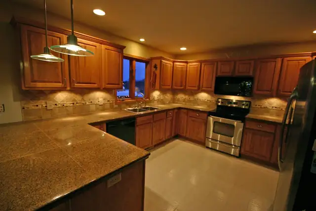 Traditional kitchen with wood cabinets, granite counters, stone backsplash and pendant lights