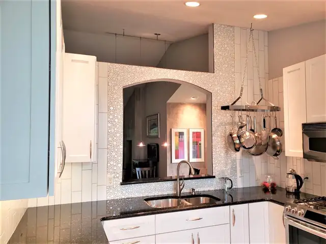 White kitchen with an arched pass-through, white mosaic tile wall, black countertops and a hanging pot rack