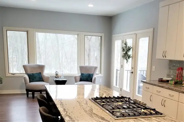 Kitchen with a granite island and gas cooktop, white cabinets and large windows over a sitting area