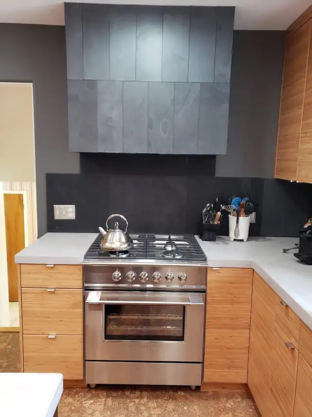 Kitchen with warm wood cabinets, stainless range, dark tile backsplash and a slate-gray range hood