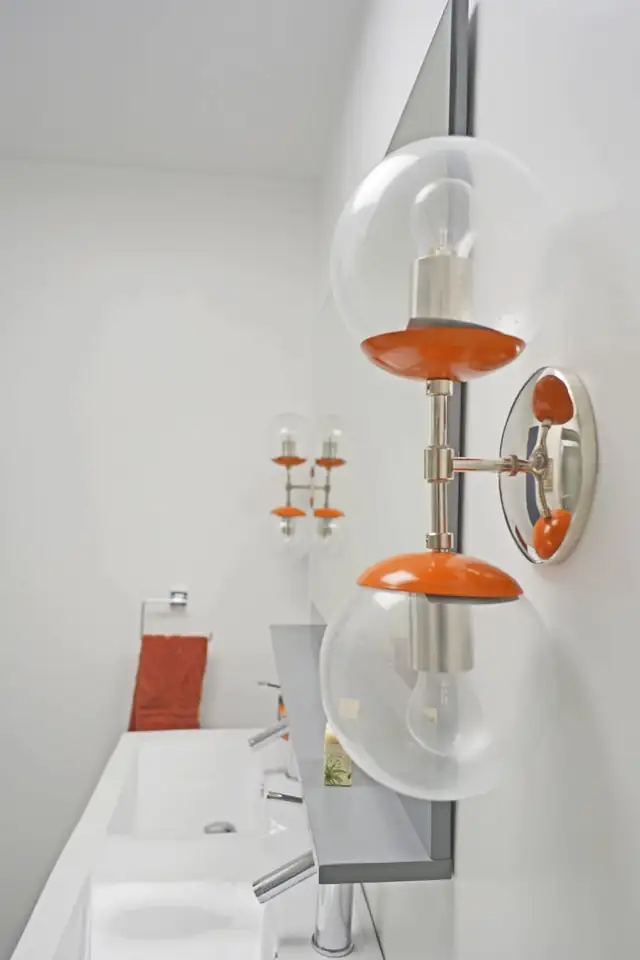White bathroom with a double sink vanity and globe wall sconces with orange accents